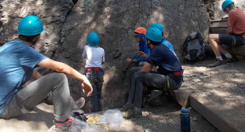 a teen belays during a rock climbing exercise while several others look on